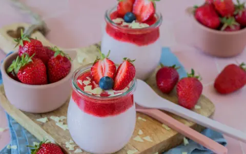 Zwei Gläser mit cremigem Joghurt und Erdbeersoße, garniert mit frischen Erdbeeren und Blaubeeren. Ein schneller Nachtisch mit Erdbeeren, der Lust auf mehr macht.