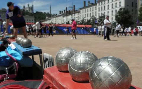 Boules de jeu en gros plan, prêtes pour une partie de boule lyonnaise. Des joueurs s'affrontent en arrière-plan.