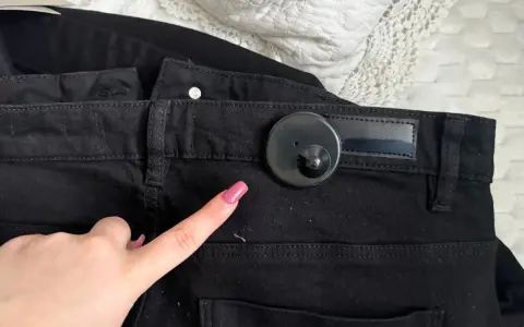 Palec wskazujący z różowym lakierem zbliża się do czarnego klipsa magnetycznego na spodniach. Dowiedz się, jak ściągnąć klips magnetyczny z ubrania.