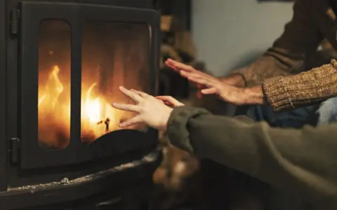 Manos calentándose frente a una chimenea con llamas danzantes. Los tubos de aire de la chimenea ayudan a distribuir el calor.