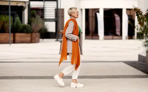 Coole Frauen mit 50: Stilvoll in kariertem Blazer, orangefarbenem Schal und weißen Hosen.