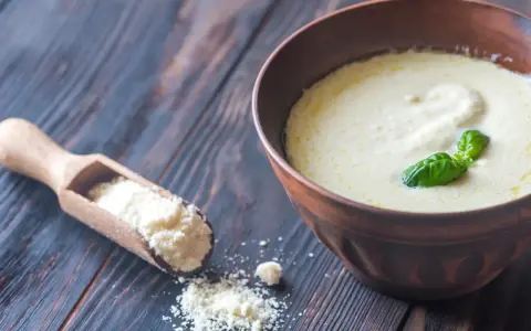 Sauce crémeuse à la sauce parmesan italienne, garnie de basilic frais. Une cuillère en bois contient du parmesan râpé.
