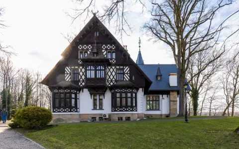Pałac myśliwski w Promnicach, z charakterystyczną architekturą szachulcową i zdobieniami, otoczony drzewami.