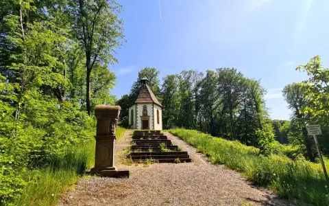 Ein kleiner Weg führt zu einer Kapelle auf einem Hügel, umgeben von grünen Bäumen. Der schmetterlingspfad willebadessen lädt zum Entdecken ein.