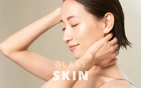 Kobieta z idealną, lśniącą cerą typu "glass skin", z dłońmi przy szyi i ramieniu.