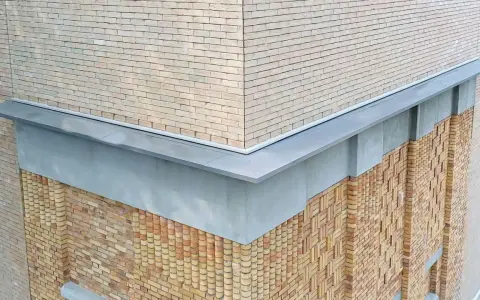 Narożnik budynku z ceglaną elewacją i nowoczesną attyką. Detale architektoniczne podkreślają fakturę muru.