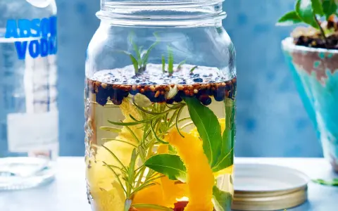 Ein Glas mit Zutaten für ein Sloe Gin Rezept: Wacholder, Zimt, Zitronenschale, Rosmarin und Lorbeerblätter in Alkohol.