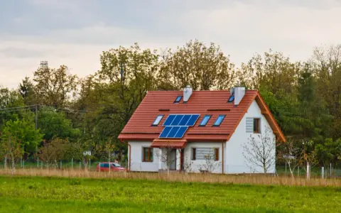 Nowoczesny dom energooszczędny z panelami słonecznymi na dachu, otoczony zielenią.