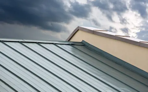 Dunkle Wolken über einem modernen Metalldach. Die glänzenden Aluminiumbahnen reflektieren das Licht, doch die Nachteile wie Geräuschentwicklung bei Regen sind nicht sichtbar.