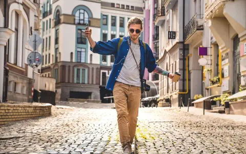 Giovane con caffè e smartphone cammina in città su un selciato, godendosi la musica e il paesaggio urbano.