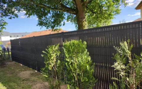 Clôture ajourée noire, offrant une protection discrète pour les tuyaux PVC. Des arbustes verts bordent cette barrière moderne.