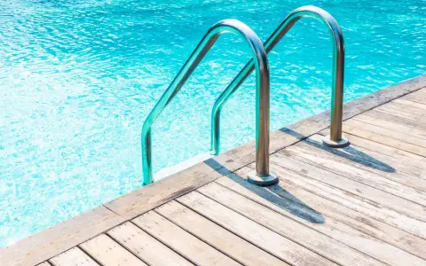Escalera de piscina de obra con barandillas cromadas sobre tarima de madera. ¿Cuánto cuesta una piscina de obra?