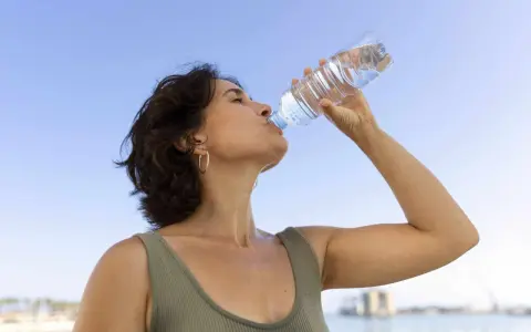 Donna beve acqua per combattere il caldo e la depressione, con il cielo azzurro sullo sfondo.