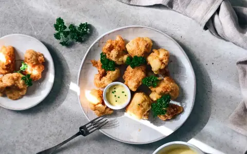 Crujientes trozos de coliflor rebozada, servidos con una cremosa salsa y decorados con perejil fresco. ¡Un aperitivo delicioso!