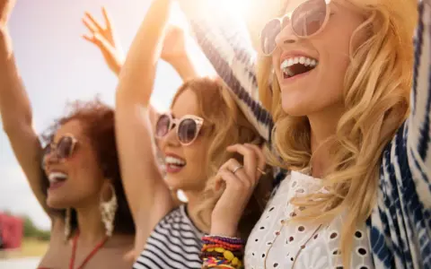 Trois amies profitent d'un festival ensoleillé, leurs rires atteignant un niveau sonore équivalent à 66 décibels.