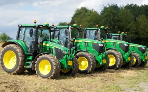 Rząd zielonych traktorów John Deere z żółtymi felgami na polu. Widać ich charakterystyczny wygląd i potężne opony.