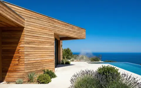 Maison moderne aux parements en bois de douglas ou pin, avec piscine à débordement et vue sur la mer.