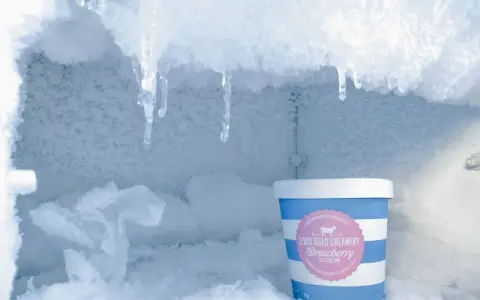 En burk jordgubbsglass står i en frys full av frosta av frys. Isformationer hänger från taket.