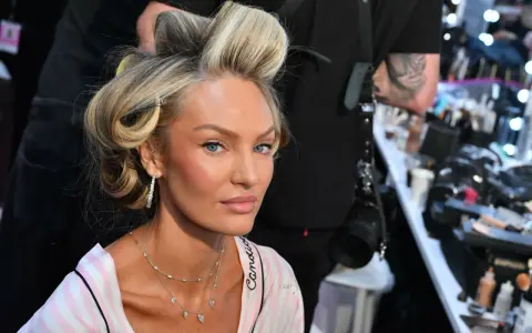 Blond włosy modelki w lokach, delikatny air touch. W tle wizażystka i kosmetyki.
