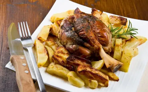 Stinco di maiale arrosto con patate croccanti, guarnito con rosmarino fresco. Un piatto succulento pronto per essere gustato.