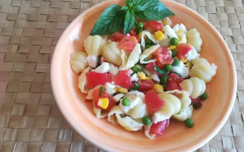 Un'appetitosa insalata di pasta vegetariana con pomodorini, piselli, mais e mozzarella, guarnita con basilico fresco.