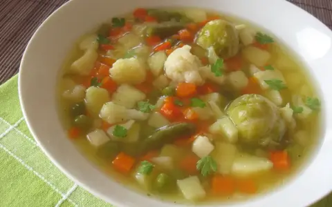 Aromaticzna jarzynowa zupa z ziemniakami, marchewką, kalafiorem i brukselką, udekorowana natką pietruszki.