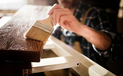 Un artesano aplica barniz a la madera con una brocha, resaltando su veta y dándole un acabado protector.