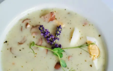Aromaticzny żurek z kiełbasą i jajkiem, ozdobiony gałązką lawendy i kiełkami.