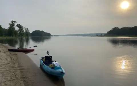 Två kajaker vid en sandstrand, redo för en paddling. Solen lyser svagt genom diset. Frågan är hur långt paddlar man på en dag?