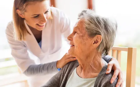 Młoda opiekunka wspiera uśmiechniętą starszą panią, która jest chora na alzheimera.
