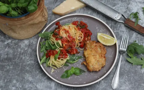Piccata Milanese: goldbraunes Schnitzel mit Spaghetti in Tomatensauce, garniert mit Rucola und Zitrone.