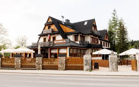 Szukasz miejsca, gdzie zjeść w Kościelisku? Ta restauracja z drewnianym ogrodzeniem i białymi parasolami zaprasza na góralskie smaki.