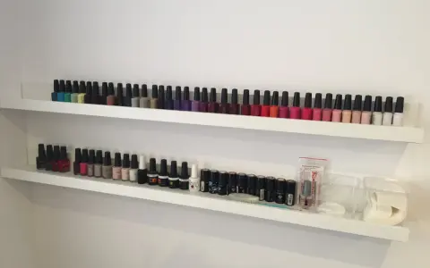 Dwie białe półki wypełnione po brzegi kolorowymi buteleczkami. To idealna półka na lakiery dla każdej miłośniczki manicure.