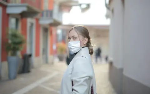 Kobieta w masce na twarzy, zastanawia się, ile można być na L4, idąc ulicą.