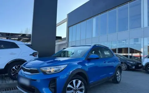 Błękitny Kia Stonic 2023 zaparkowany przed salonem samochodowym. Obok stoi biały SUV.