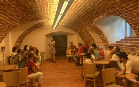 Grupa zwiedza piwnice pałacu w Poddębicach. Przewodniczka opowiada o historii miejsca.