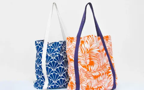 Deux sacs fourre-tout aux motifs vibrants : un bleu avec des éventails blancs, l'autre orange avec des feuilles de palmier blanches. Un patron de sac gratuit à télécharger pour créer vos propres accessoires.