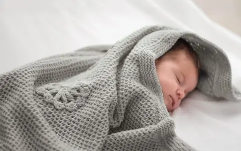 Ein schlafendes Baby, eingewickelt in eine gestrickte Babydecke mit Blumenmuster. Eine Anleitung zum Babydecke stricken wäre hier perfekt.