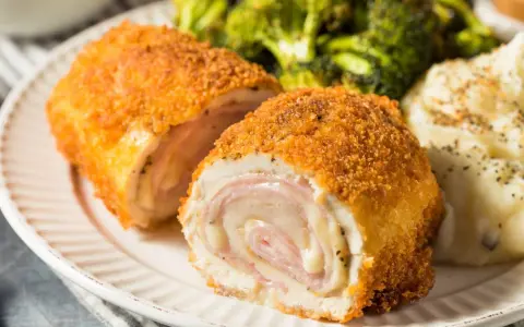 Schab po szwajcarsku, chrupiący panierowany kotlet z serem i szynką, podany z puree ziemniaczanym i brokułami.