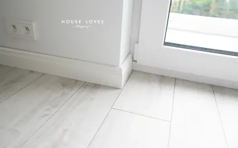 Białe listwy przypodłogowe przy oknie balkonowym, na jasnej podłodze.