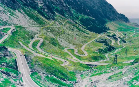Kręta droga Transalpina wijąca się po zielonych zboczach gór. Widok z lotu ptaka na serpentyny i mosty.