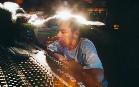 Un disc jockey célèbre, concentré, manipule une console de mixage dans un studio d'enregistrement, baigné de lumières vives.
