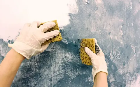 Händer med handskar målar akryl med svamp på en vägg för att skapa en texturerad effekt.