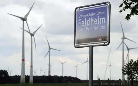 Schild "Energieautarker Ortsteil Feldheim, Stadt Treuenbrietzen" vor vielen Windrädern in Brandenburg.