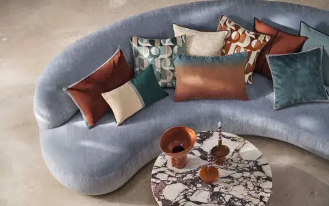 Sofá curvo gris con cojines de terciopelo y estampados geométricos. Un diseño moderno y acogedor.