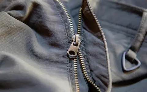 Detalle de una cremallera de chaqueta que se ha salido, mostrando el cursor metálico y los dientes.
