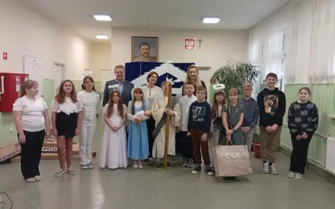 Dzieci w strojach aniołów i pasterzy, odgrywające baśń o dobrym synku. W tle portret i dekoracje.