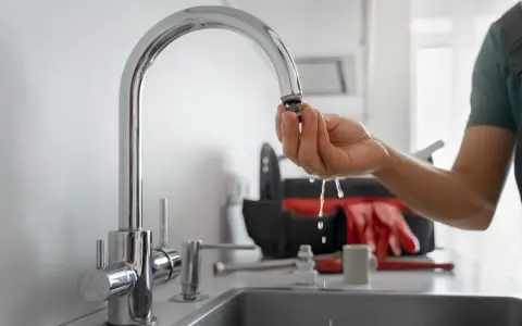 Dłoń trzymająca wyczyszczony aerator kranu, z którego kapie woda.