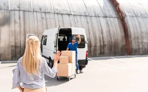 Kobieta macha do kuriera, który właśnie zakończył studia transportowe i dostarcza paczki.