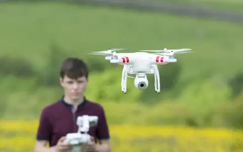 Ein Junge steuert eine Drohne in Litauen. Die Drohne schwebt über einem Feld mit gelben Blumen.